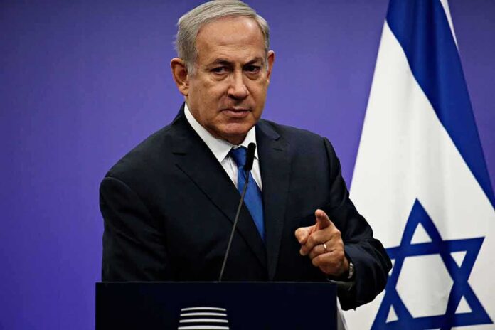 shutterstock_1042782061 man in suit speaking at a podium with an Israeli flag