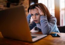 Championship Hype Turned Corporate Trap – Workers Outraged Woman holding her head while looking at a laptop