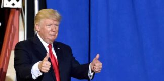 Donald Trump giving two thumbs up in front of a blue curtain