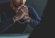 man in handcuffs resting clasped hands on table