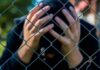 ICE Death Chaos: Detainee Begged For Meds Person behind chain-link fence holding head in hands