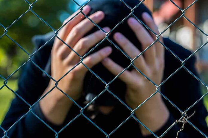 Person behind chain-link fence holding head in hands