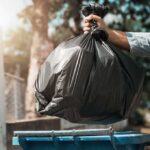 City Cleans House – Nightmare Crawls Back Hand dropping a black garbage bag into a blue bin