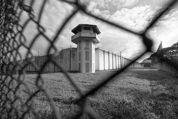shutterstock_1469991386 Prison watchtower behind chain-link fence