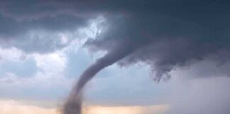 Tornado touching down over open farmland under dark storm clouds