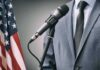 Microphone at podium with person in suit and US flag