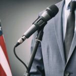 Debate Meltdown – Hilton Hit With Explosive Race Charge Microphone at podium with person in suit and US flag
