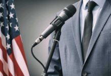 Debate Meltdown – Hilton Hit With Explosive Race Charge Microphone at podium with person in suit and US flag