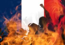 Racist Terror Label – Macron’s “First-Ever” Claim Sparks Fury silhouetted crowd and flames before a French flag