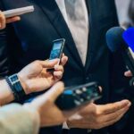 Congressman Threatens Student Reporter With Prosecution businessperson in suit surrounded by microphones and recorders