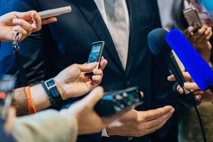 shutterstock_471987556 businessperson in suit surrounded by microphones and recorders
