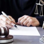 DOJ Alleges Livestreamed School Slaughter Plan Judge writing at desk with gavel and Lady Justice statue